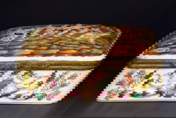 CAPODIMONTE ITALY PORCELAIN PUTTI HINGED BOX: Depicts dancing putti in a landscape scene. Sides depict putti in a Florentine-like pattern. Has bronze hardware. Hand painted flowers on interior. Has blue crown mark to bottom. Measures 2 3/8"" h X