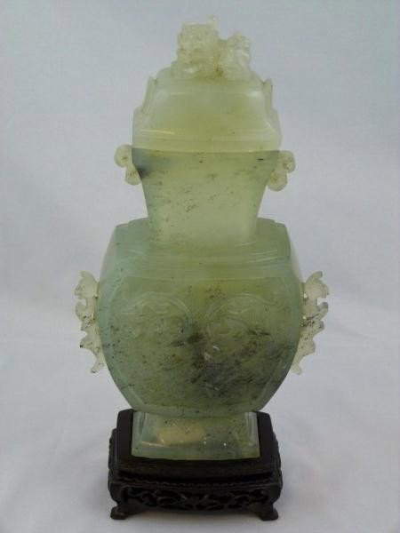 CHINESE CELADON JADE FOO DOG COVERED URN: Handles have a figural dragon design. Front and back of the vase have a raised floral design. Cover is a figural carved foo dog design. No apparent signature. 19th or early 20th century. Notice the be