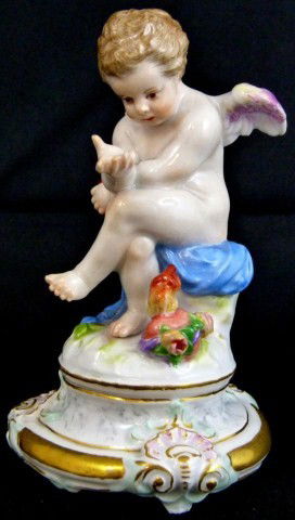 MEISSEN GERMAN PORCELAIN CHERUB FIGURE M103: Meissen cherub figure symbolizing love. He is holding a heart. A flaming heart is on the floor next to his foot. Blue Meissen crossed swords mark to bottom. Impressed M103 and 34. Late 19th or early 2