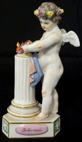 MEISSEN GERMAN PORCELAIN CHERUB FIGURE F1: Meissen figure of a cherub standing next to a pillar and tying two hearts together as one. Has a triangular shaped base with pink panels, one inscribed "Je les unis". Blue crossed swords mark to botto