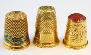 18k YELLOW GOLD THIMBLES - LOT OF 3: Three yellow gold 18kt thimbles. The first has floral enameling to bottom and knurling pattern to top and side. Marked 18k and "9". Measures 13/16" (21mm)height. The second has a chased design with am