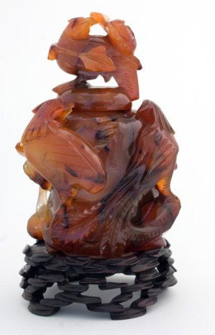 HEAVILY CARVED CARNELIAN AGATE JAR w LID: Heavily carved carnelian agate jar with finial lid. Depicts birds and flowers. Has wooden base. Measures 6" height x 4" width. 19th century.