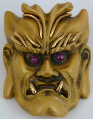 14kt YG CHINESE CARVED IVORY THEATER MASK PENDANT: 14kt yellow gold bail and detail on forehead, eyebrows and teeth. Scowling face. Round ruby cabochon eyes. Color is medium "goldish". Two holes drilled through top of head for chain. Weighs 19.8dwt (3