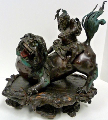 ANTIQUE BRONZE FIGURE DEPICTING WARRIOR ON FOO DOG: Depicts a fat warrior with shuriken in right hand and riding on a foo dog. Antique Japanese cold painted bronze circa 1900. Has wooden stand. Measures 12" height + 4 3/8" base (30.4cm x 11.1cm).