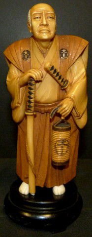JAPANESE IVORY SAMURAI WITH LANTERN FIGURE: Depicts an old Samurai with a Katana in right hand and a lantern in his left hand. He is wearing layered robe. Signed to plaque on back. 19th/20th century. Measures 7" height (17.7cm).