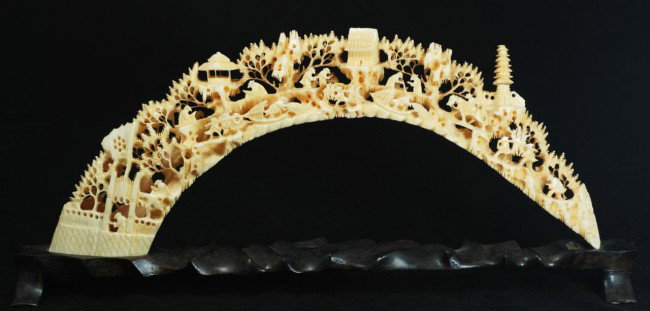 CHINESE CARVED IVORY VILLAGE TUSK: Antique Chinese hand carved village tusk. Has very intricate hand carved village scene. Depicts trees, pagodas, boats, and villagers. 19th century. Includes fitted wooden base. Measures 5 1/4" height 