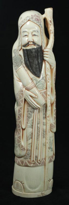CHINESE CARVED IVORY FIGURE OF BEARDED MAN: Hand carved Chinese ivory figure depicting a man with wooden staff. In his right hand is a Scroll. He is wearing layered robe and head dress with intricate polychromed flowers, patterns, calligraphy a