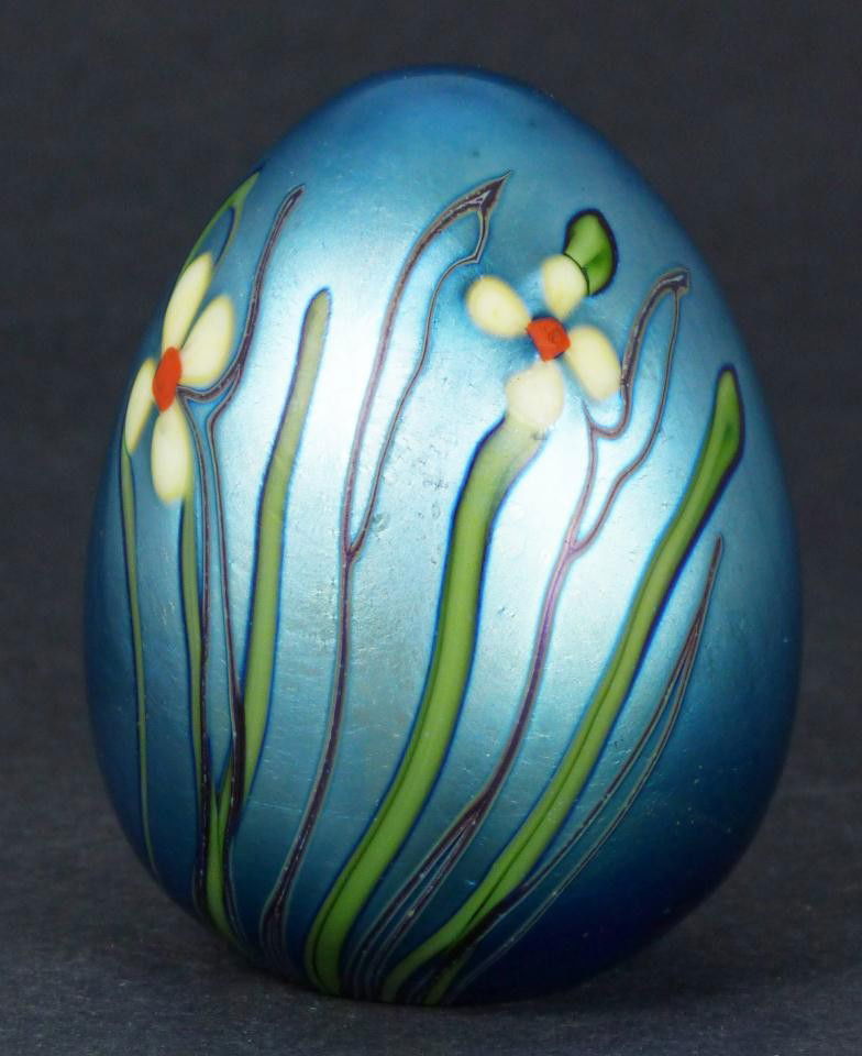 ORIENT & FLUME IRIDESCENT GLASS EGG PAPERWEIGHT: Orient and Flume iridescent egg shaped paper weight with floral designs. Has original paper sticker to bottom. Signed to edge of bottom and dated 1976. Made in Chico, California. Measures 3" height (7