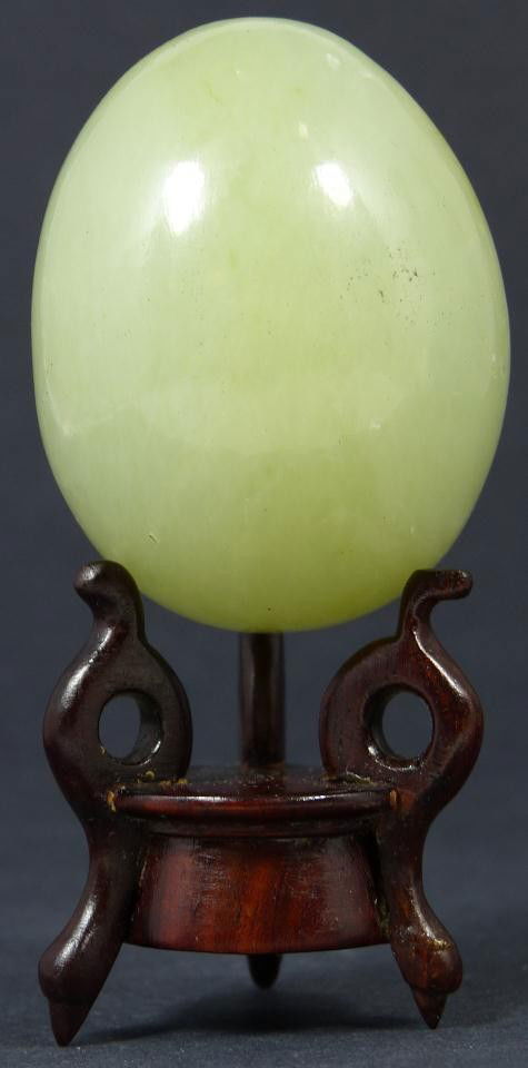 CHINESE CARVED JADE EGG ON WOOD STAND: Hand carved Chinese jade egg. Has smoothed exterior. Includes fitted wooden stand. Egg measures 2 1/2" height + 1 3/8" base height (6.3cm + 3.4cm).