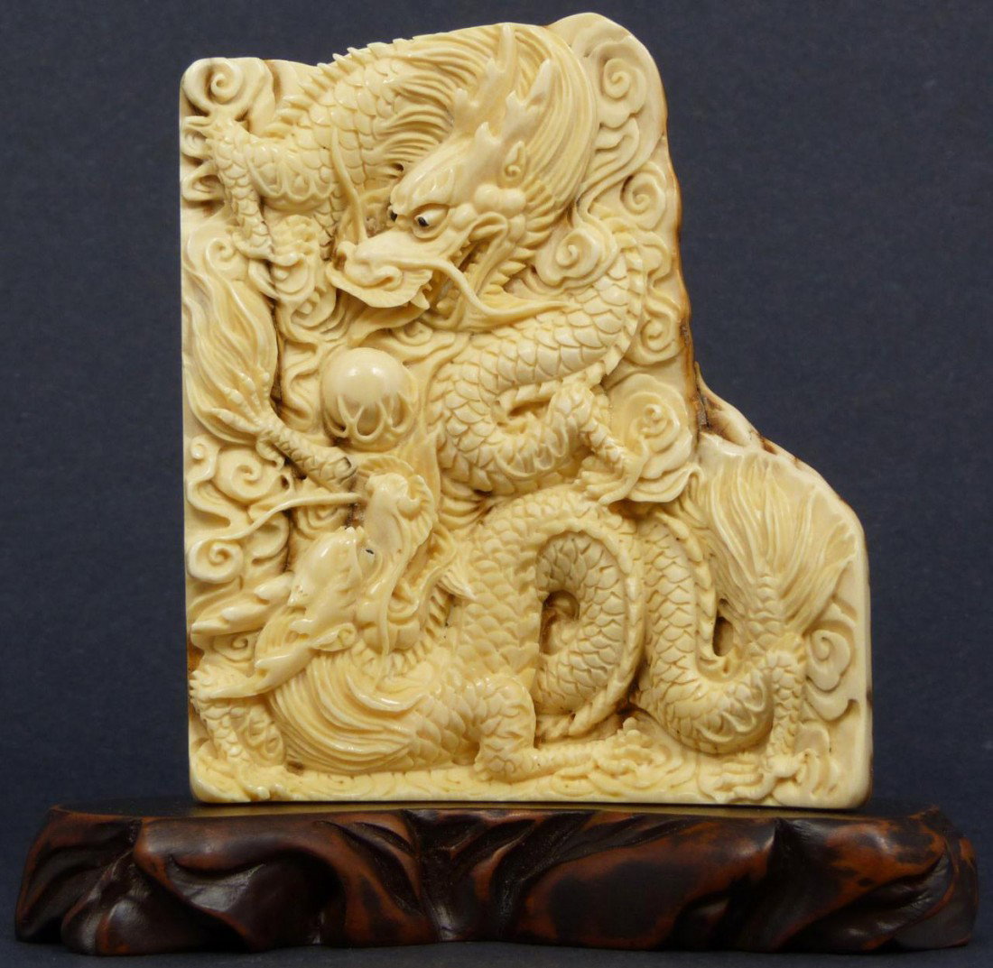 CHINESE CARVED MAMMOTH IVORY DRAGON PLAQUE: Hand carved Chinese Mammoth tusk ivory dragon plaque. Has detailed relief carving depicting two dragons with a dragon jewel. Signed to bottom. Measures 3 7/8" height x 6 1/2" width + 5/8" base height 