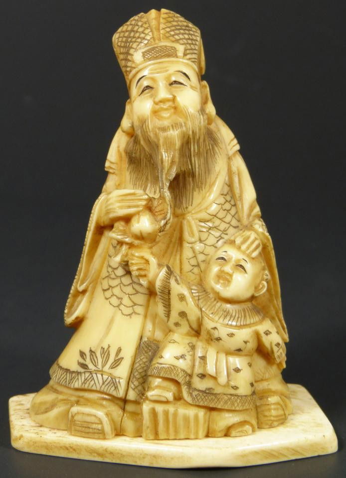 JAPANESE CARVED IVORY FIGURE OF WISEMAN & CHILD: Hand carved Japanese ivory hand carved group figure depicting a wise man with child. The child is handing the older man a peach. Signed to bottom. 19th century. Measures 3 1/4" height (8.2cm).