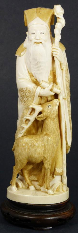 JAPANESE IVORY FIGURE OF SHEPHERD SIGNED FAN: Japanese hand carved figure depicting a wiseman holding wooden staff and scroll. At his feet is is a young stag. Signed to red plaque to bottom "Fan". Measures 9 1/8" height + 1 1/8" height (23.1cm + 