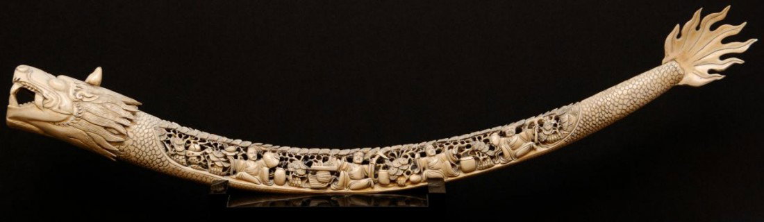 19th C. CHINESE CARVED IVORY DRAGON TUSK: Antique hand carved Chinese ivory dragon tusk. Has a fully reticulated design depicting 8 merchants selling wares. Also in the scene is trees, fruit and leaves. 19th century. Includes fitted wooden pr
