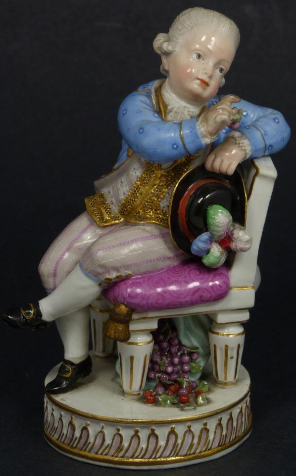 MEISSEN PORCELAIN FIGURE OF BOY OFFERING GRAPES: Antique Meissen German porcelain figure. Hand painted porcelain seated male figure dressed in grey wig, blue waist coat and gilt vest gripping black plumed hat handing grapes to unknown receiver. The 