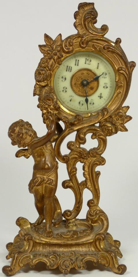 19th C. FRENCH BRONZE CHERUB MANTLE CLOCK: Antique dore bronze figural cherub clock. Has white enamel face with black enamel Arabic numerals and notches. Beautiful scroll design throughout. Measures 8 1/8" height (20.6cm).