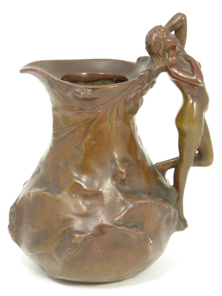 JEAN GARNIER ANTIQUE FIGURAL NUDE BRONZE: Jean Garnier (FRENCH, 1853-1910) figural nude pitcher. Body has raised root and leaf design. Figural nude female design to handle. Signed to side J. Garnier. Solid and heavy pitcher. Measures 7" heigh