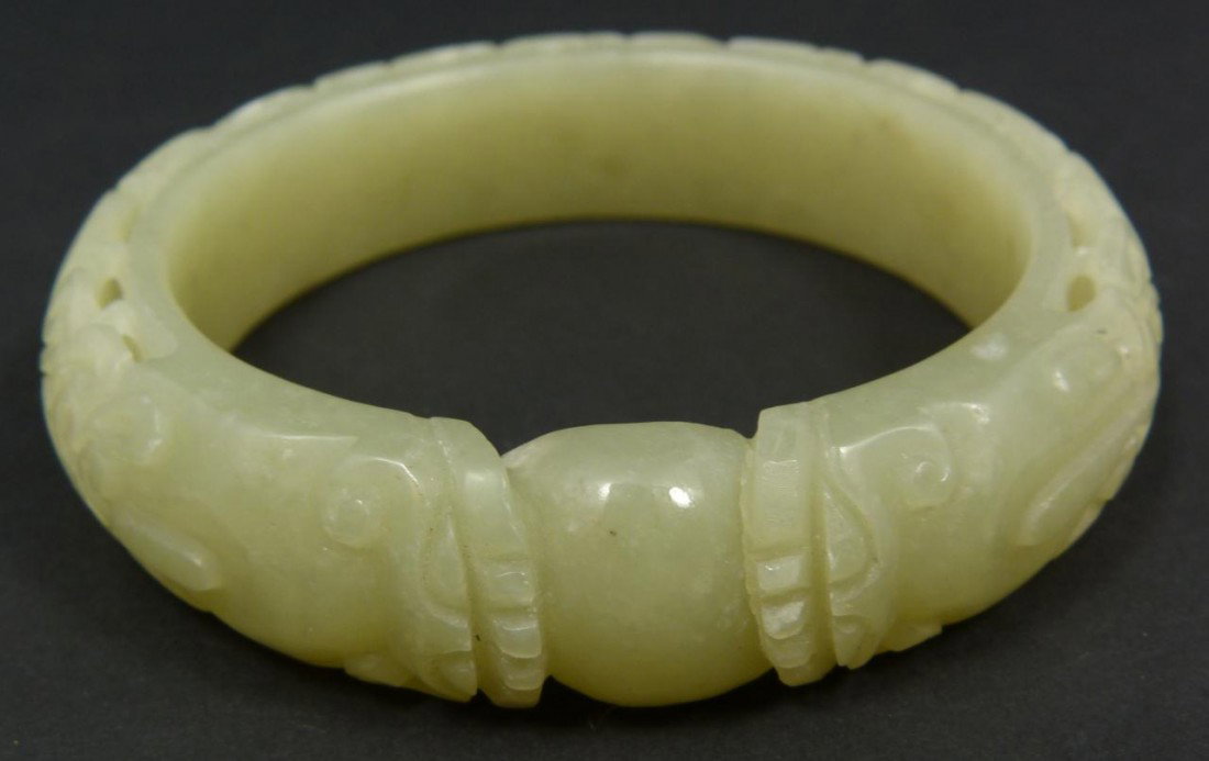 CHINESE RELIEF CARVED JADE DRAGON BANGLE BRACELET: Finely carved Chinese pale green jade bangle bracelet. Has a layered relief carved scrolled design with bats and two dragon heads flanking a dragon jewel. Beautiful translucence to jade. Measures 3" d