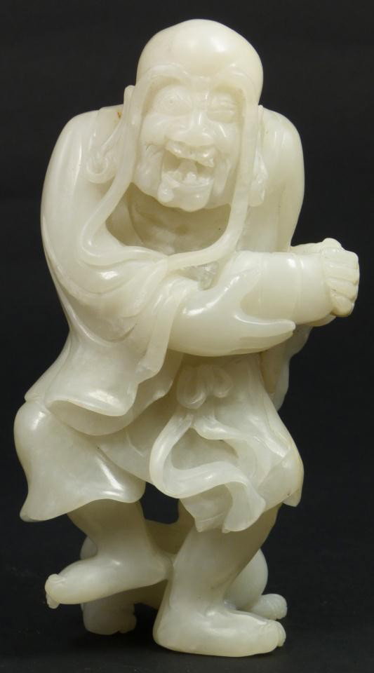 CHINESE CARVED WHITE JADE FIGURE OF OLD MAN: Chinese hand carved white jade figure of old man. He is holding a bowl in his hands and showing an eerie grin. He has long eyebrows and pierced ears. He is wearing layered robe with dog companion tugg