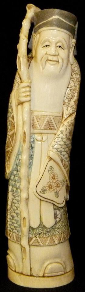 JAPANESE CARVED POLYCHROME IVORY FIGURE OF SHOU: Hand carved Japanese ivory figure depicting the Taoist deity of Longetivity and part of the "Three Lucky Stary Gods". The figure depicts the deity frowning with paddle fan pointed down and held in lef