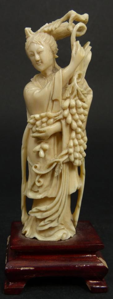 CHINESE CARVED IVORY FIGURE OF MAIDEN w GRAPES: Chinese hand carved ivory figure depicting standing maiden holding berry clusters on vines. She is depicted in flowing robe with Phoenix head dress. Set to wooden base. Measures 5" height + 1 1/8" bas