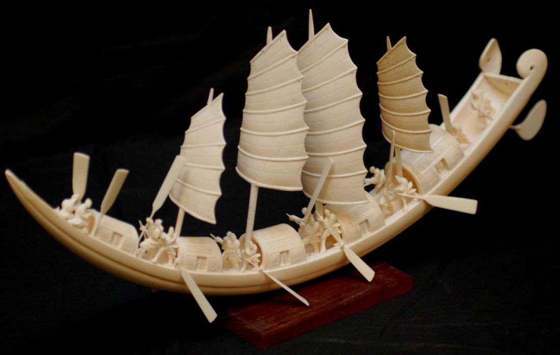 CHINESE HAND CARVED IVORY ELEPHANT TUSK BOAT: Chinese hand carved ivory boat figure. Boat depicts 16 figures, 4 masts and sails with 8 oars. Also includes rudder. Set on wooden base. Measures 12" height x 28" length + 3/4" base height (30.4cm x 7