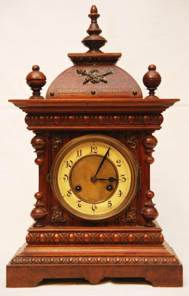 J. UNGHANS GERMAN WALNUT BRACKET CLOCK: 19th century J. Unghans German bracket clock with walnut case. Torch and quiver in wreath design over brick pattern to top with 3 spires. Has bronze and enamel face with black Arabic Numerals. Black h