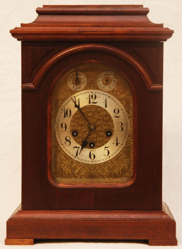 JUNGHANS GERMAN MAHOGANYMANTLE CLOCK: Old Junghans Germany mahogany mantle clock. Has chased brass face floral design throughout. Has black enameled Arabix numbers to face. Beveled glass screen to front door. Has tiered case design. Movem