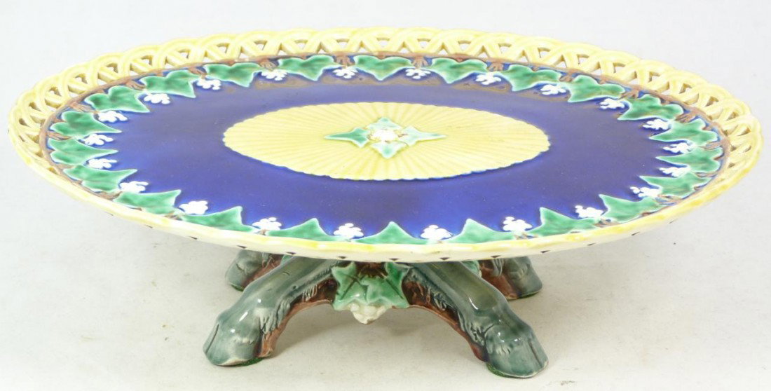 ANTIQUE WEDGWOOD MAJOLICA PORCELAIN CAKE STAND: Antique Wedgwood English majolica porcelain cake stand. Has reticulated design to rim with floral inner border over cobalt background. Has ovoid shape to plate and figural hoof legs to base. 19th cent