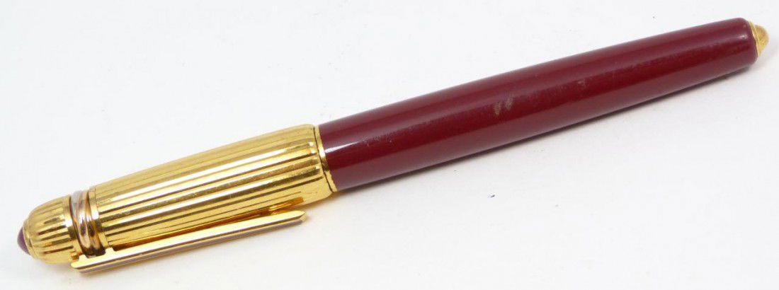 CARTIER TRINITY ROLLER BALL PEN WITH CABOCHON RUBY: Pasha de Cartier 18k yellow gold plate Trinity bordeaux roller ball pen having ruby cabochon spinel. Completed with 18k yellow gold finish. Marked 1988 1796. Includes original Cartier suede cover slee