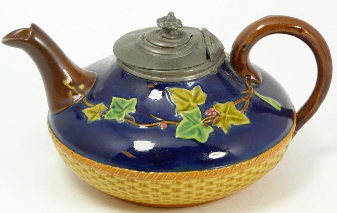 ASTON MAJOLICA LOW BASKET WEAVE TEAPOT: Antique Aston Majolica earthenware low teapot with brown basket weave and cobalt design and raised floral designs. Has hinged pewter cover. Holds raised Aston globe mark with registration mark. 19th c