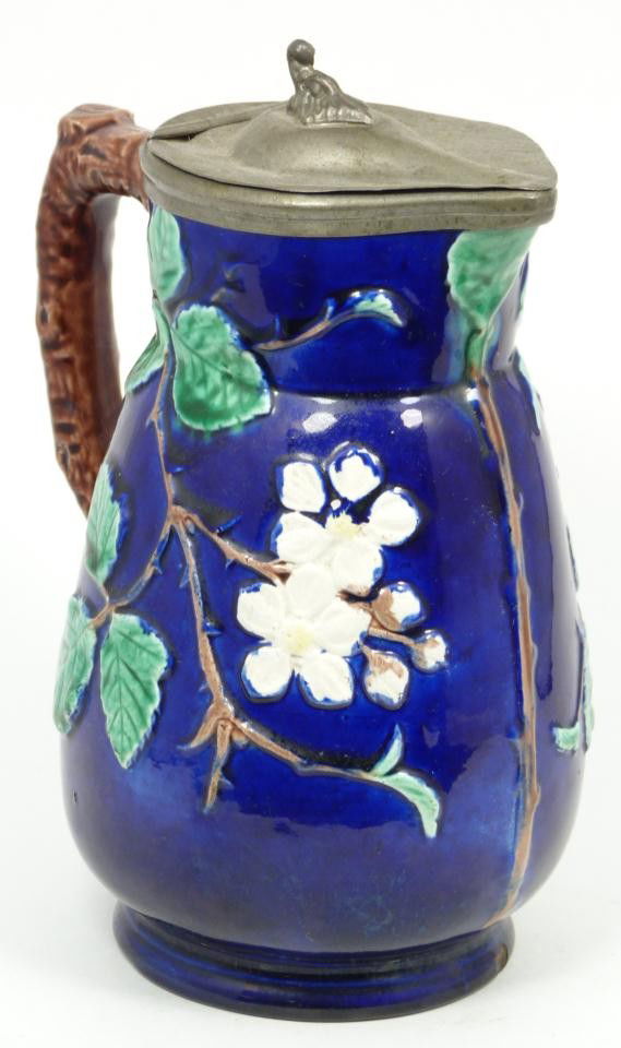 BLUE COBALT FLORAL ENGLISH MAJOLICA PITCHER: Antique Majolica earthenware pitcher with raised floral designs throughout over cobalt background and branch form handle. Has hinged pewter cover. 19th century. Measures 7 3/8" height (18.7cm).