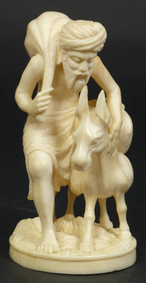 HAND CARVED INDIAN IVORY GROUP FIGURE: Hand carved Indian ivory figure depicting a man with donkey. The man and donkey are both carrying sacks of rice or grain. Includes wooden base. Measures 4" height + 1" base height (10.1cm + 2.5cm). To
