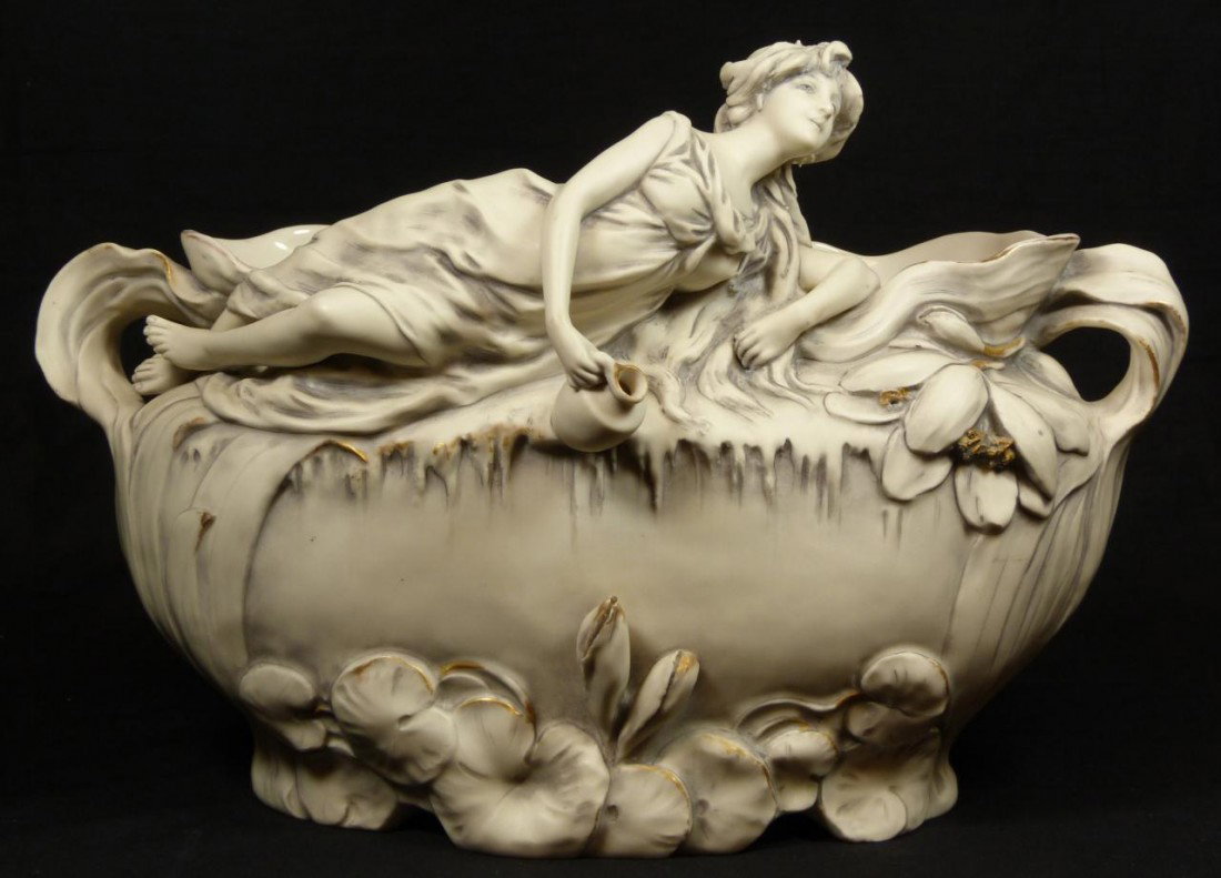 ROYAL DUX ART NOUVEAU PORCELAIN JARDINIERE BOWL: Royal Dux figural porcelain jardiniere bowl. Wide oval bowl depicts a maiden with water pitcher laying to front of rim. Raised floral designs throughout with flora form handles. Holds raised Royal Dux