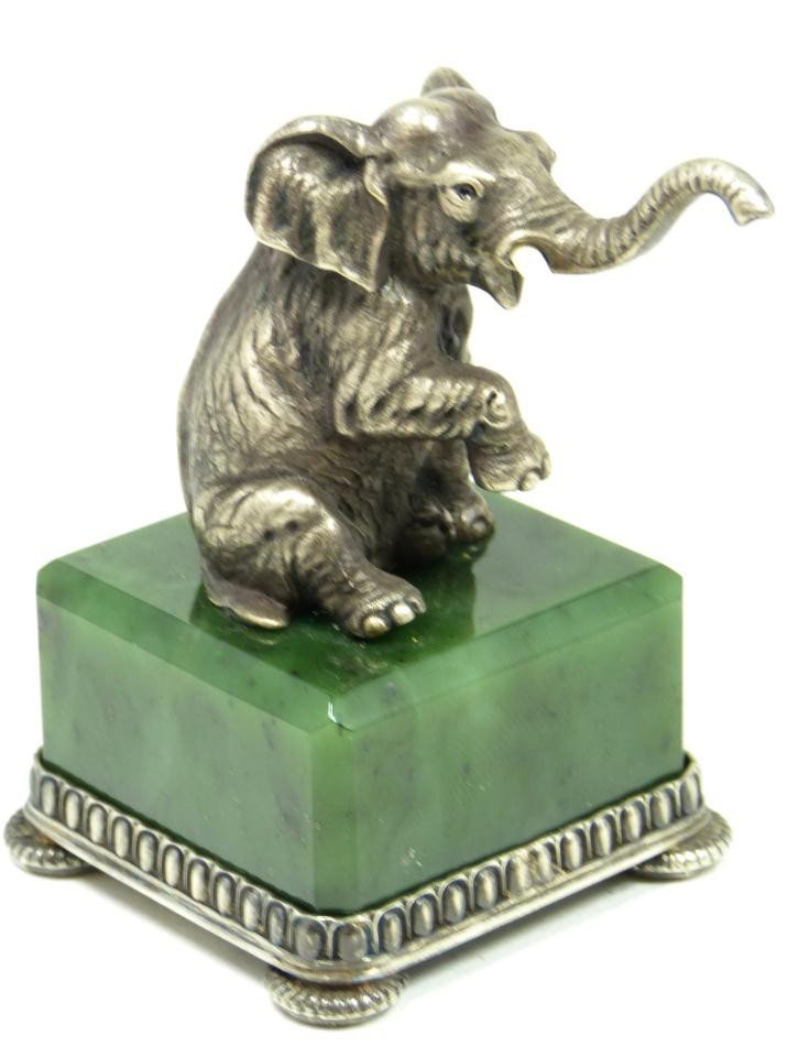 RUSSIAN SILVER & IVORY ELEPHANT ON JADE BASE: Imperial Russian silver elephant figure set on spinach green nephrite jade square base. The elephant is seated with tusk and right foot raised. Base is suspended upon four ribbed discus feet. Holds to