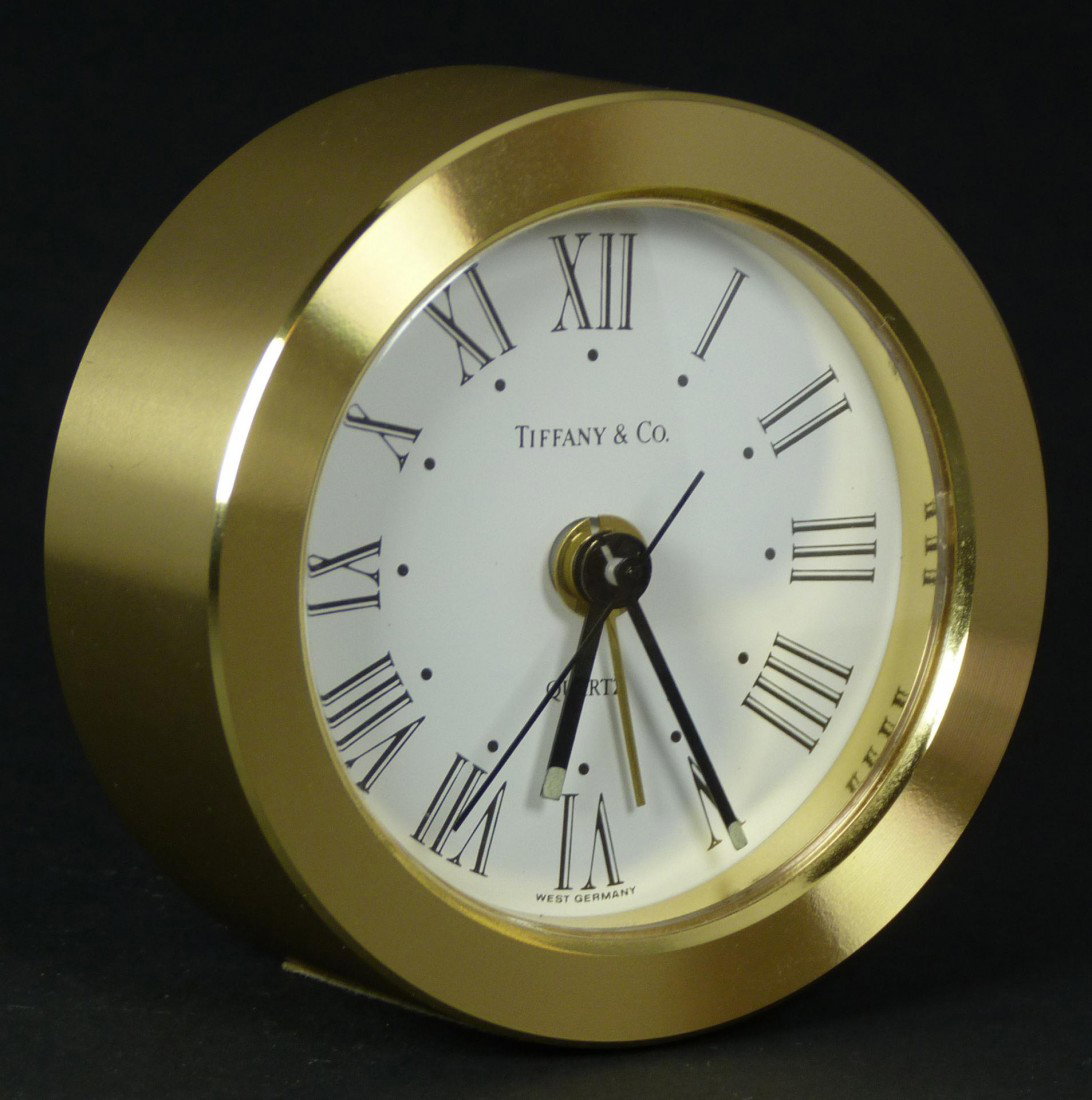 TIFFANY & COMPANY ROUND ALARM DESK CLOCK: Tiffany & Company round desk alarm clock. Has white enamel face with black Roman numerals and notches. Black hour, minute and second hands. Gold alarm hand. Quartz movement. Measures 2 3/4" diameter (