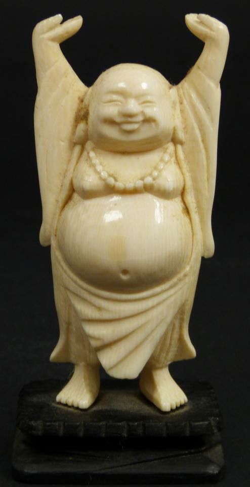 CHINESE IVORY FIGURE OF STANDING BUDDHA: Chinese hand carved ivory figure depicting standing Buddha with hands up. He is also wearing beaded necklace with elongated ears. Set to wooden base. 20th century. Measures 3 5/8" height + 1/2" height