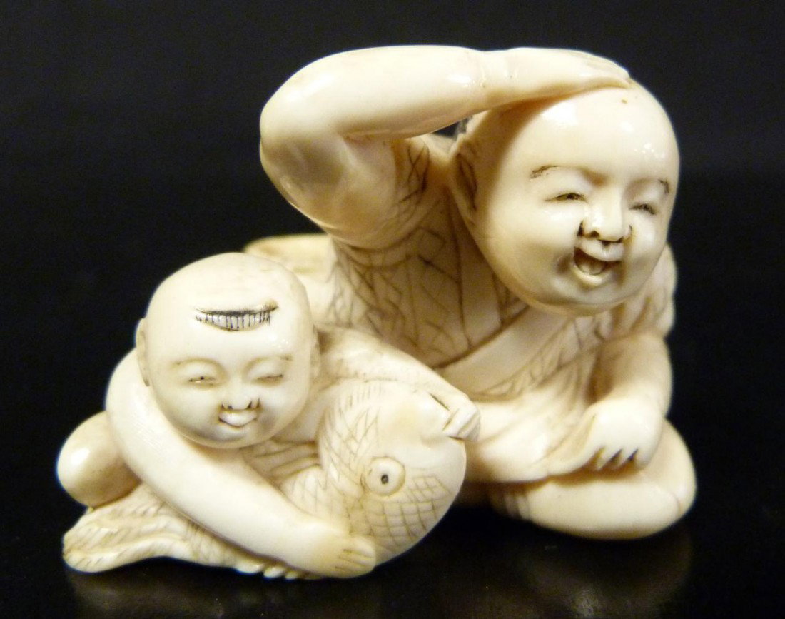 JAPANESE HAND CARVED IVORY NETSUKE OF MAN & CHILD: Japanese hand carved ivory netsuke figure depicting a man with young boy who is playing with a fish. Measures 1 3/4" length x 1 1/4" height (4.4cm x 3.1cm). Ivory weight of 31 grams.