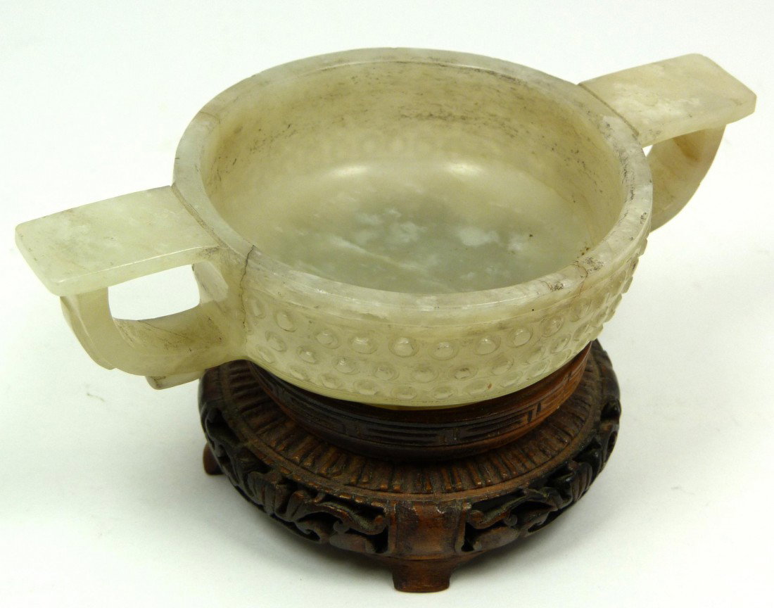 CHINESE WHITE JADE TWO HANDLED CUP: Fine Chinese white jade two handled cup having beaded design to exterior. Includes fitted wooden base. Measures 5" length x 3" depth x 1 1/4" height (12.7cm x 7.6cm x 3.1cm). Total jade weight of 130 