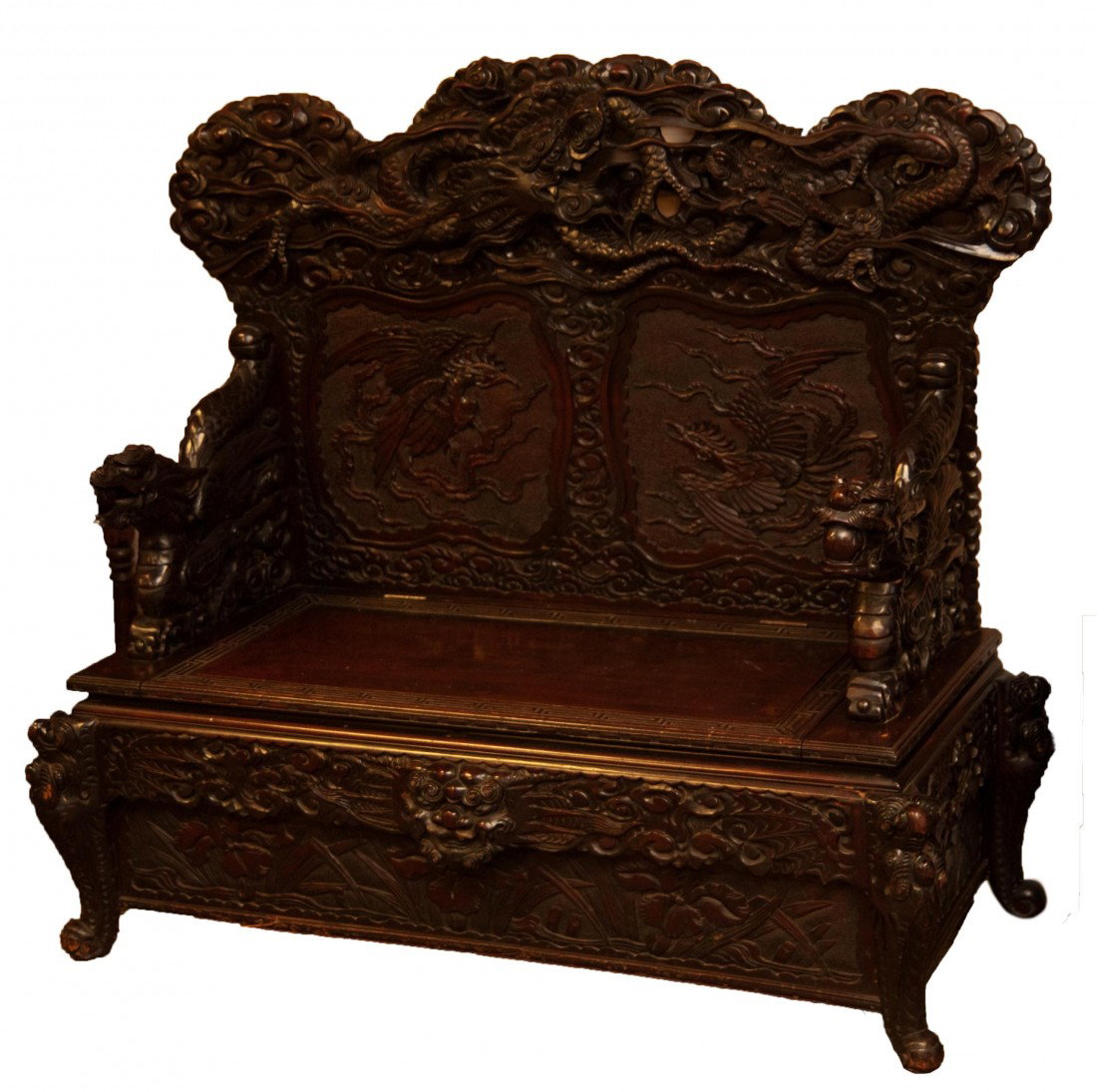 ANTIQUE CHINESE CARVED DARK WOOD STORAGE BENCH: Impressive antique Chinese hand carved dark wood storage bench, having a figural dragon arm rest design with relief carved dragon backing. Relief Etruscan pattern design to seat. Has hinged cover to c