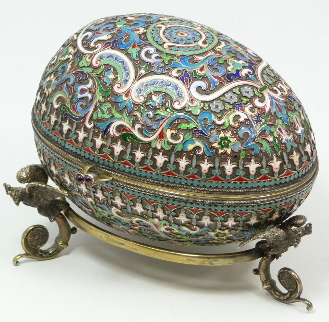 IMPERIAL RUSSIAN SILVER ENAMELED EGG OVCHINNIKOV: Large Imperial Russian silver hinged enameled egg box having elegant scrolled floral design throughout. Clasp set with two round cabochon cut garnet jewels. Gold wash interior. Includes fitted stand w