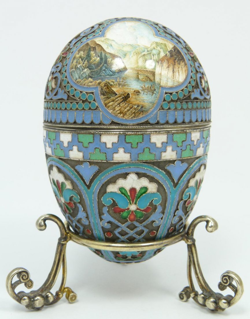IMPERIAL RUSSIAN SILVER ENAMELED EGG OVCHINNIKOV: Russian silver enameled egg box having two landscape miniatures. Gold wash interior. Includes stand with three figural plant form feet. Piece holds Cyrillic Pavel Akimov Ovchinnikov workmaster marks.