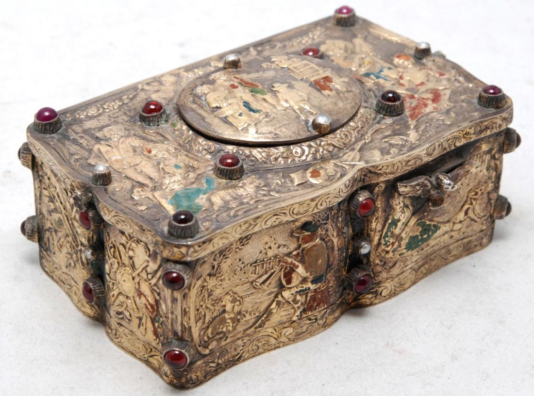 ANTIQUE GERMAN SILVER SINGING BIRD MUSIC BOX: Antique German silver bird music box with raised designs throughout depicting people singing and playing instruments. Has cabochon cut round multicolor stones throughout. Has operating switch to front