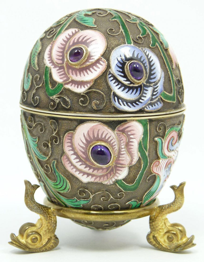 IMPERIAL RUSSIAN SILVER ENAMELED EGG KHLEBNIKOV: Russian silver enameled egg box having multicolor floral design. 6 cabochon cut sapphire jewels mounted. Gold wash interior. Includes stand with three figural pine cone feet. Piece holds Cyrillic Ivan
