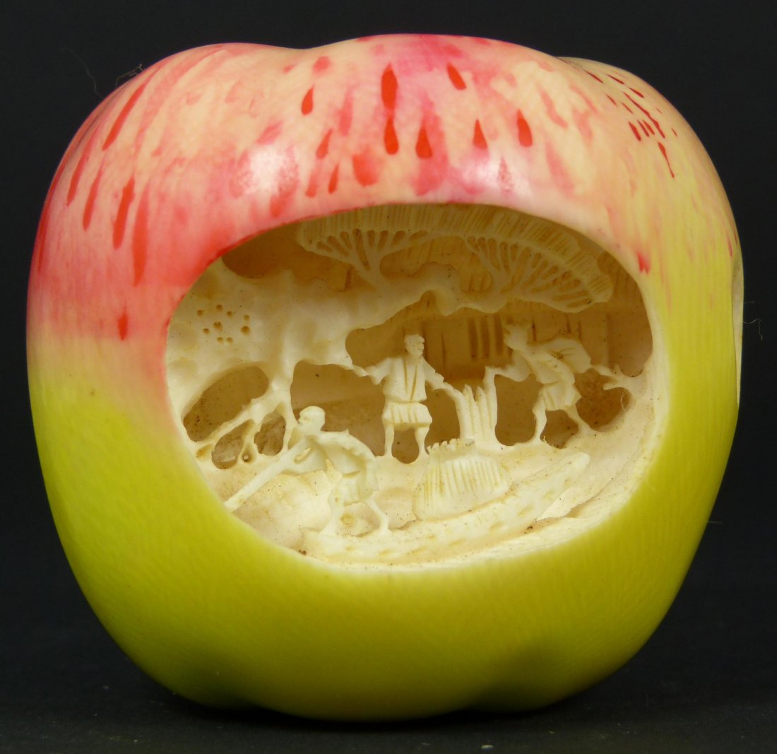 CHINESE RELIEF CARVED IVORY VILLAGE SCENE APPLE: Chinese fully relief carved apple depicting village scene with people, pagodas, trees, and boat. Beautiful green and red polychrome design to exterior. Cultural Revolution period. Signed "Guang Yu" to