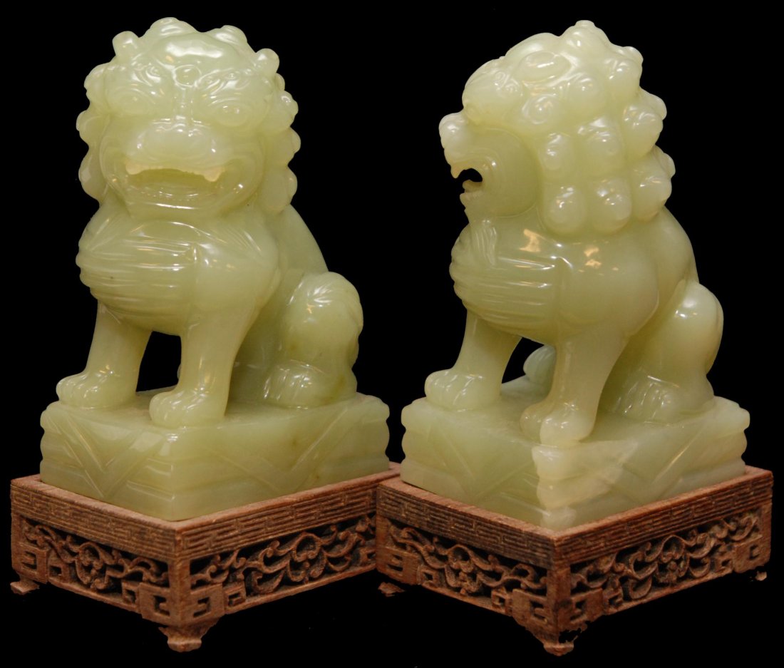 Pr CHINESE SERPENTINE JADE FOO DOG FIGURES: Pair of Chinese hand carved serpentine jade seated foo dog figures. Each depicted with both paws down. Translucent pale green jade color. 19th/20th century. Includes fitted wooden base. Each measures 
