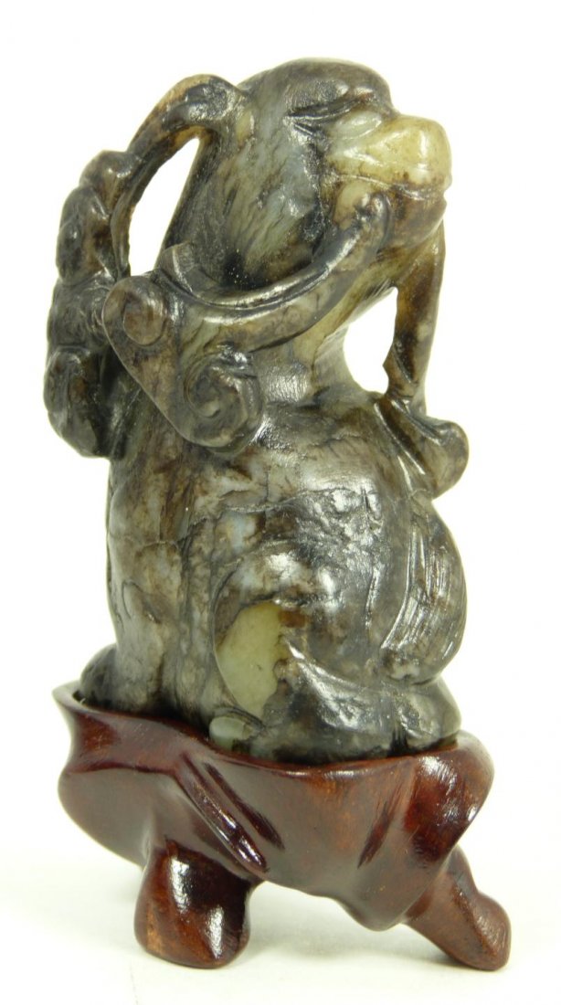 CHINESE CARVED JADE DOG FIGURE ON STAND: Chinese hand carved jade foo dog figure on stand. The foo dog is depicted in a seated position with lingzhi stalks hanging from it's mouth. Pale green jade specimen with heavy russet pebbling. Include