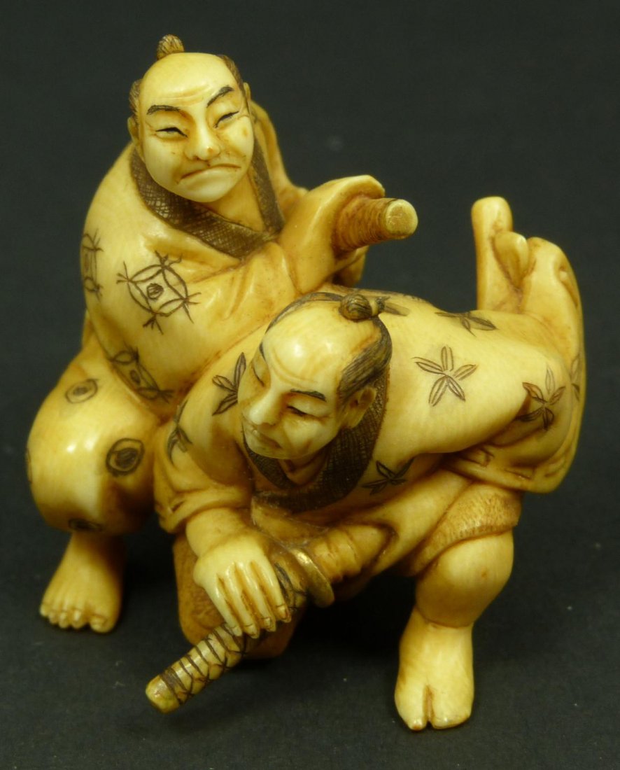 JAPANESE CARVED IVORY SAMURAI NETSUKE FIGURE: Old Japanese hand carved ivory group figure depicting two samurai readying their katana blades. High attention to detail. An inro box can be seen hanging from one of the men's belts. Signed Xiaoyue to