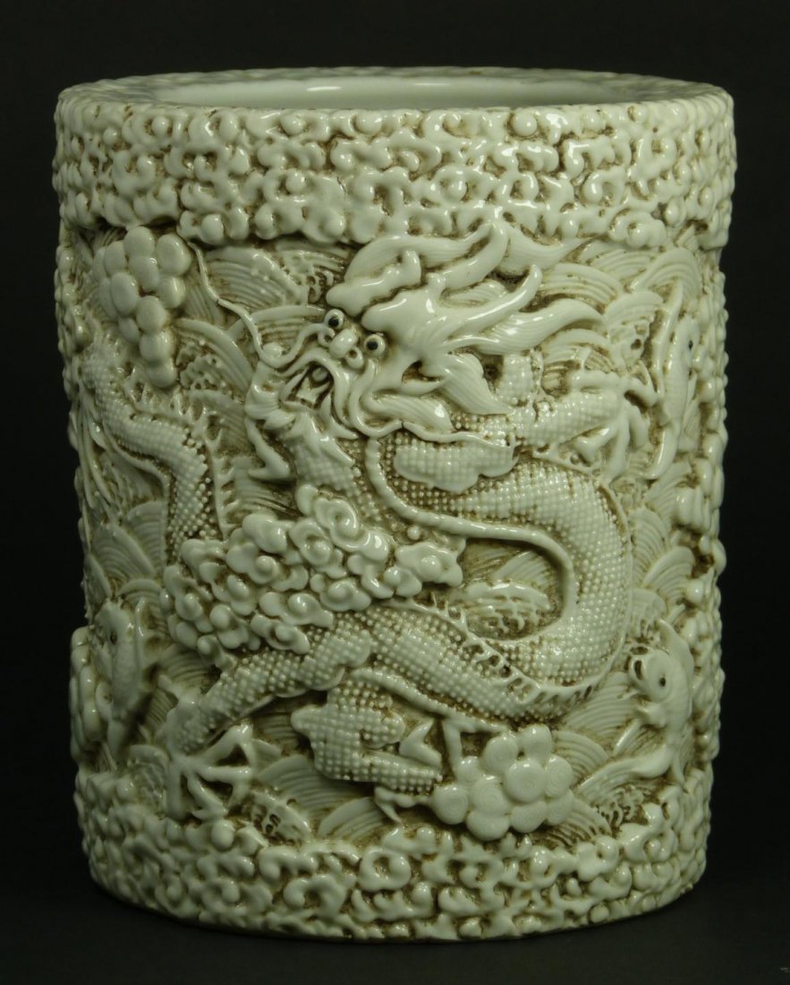 CHINESE BLANC DE CHINE PORCELAIN DRAGON BRUSH POT: Chinese blanc de chine porcelain relief brush pot depicting 2 dragons with clouds and flying fish raised over a crashing waves design. Holds Impressed four character archaic reign mark to bottom. Meas