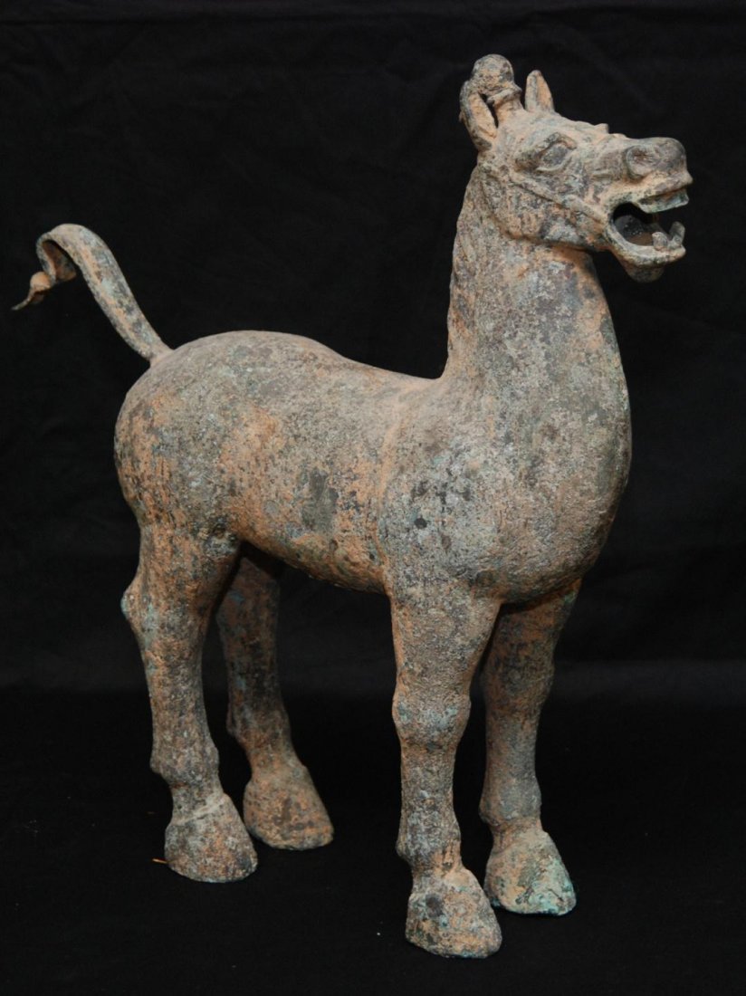 CHINESE HAN DYNASTY BRONZE HORSE SCULPTURE: Large Chinese Han Dynasty bronze horse sculpture. Depicts a standing horse with head and tail up. Has ponytail to center of top of head. Some oxidation. Measures 23" height x 22" length (58.4cm x 55.8