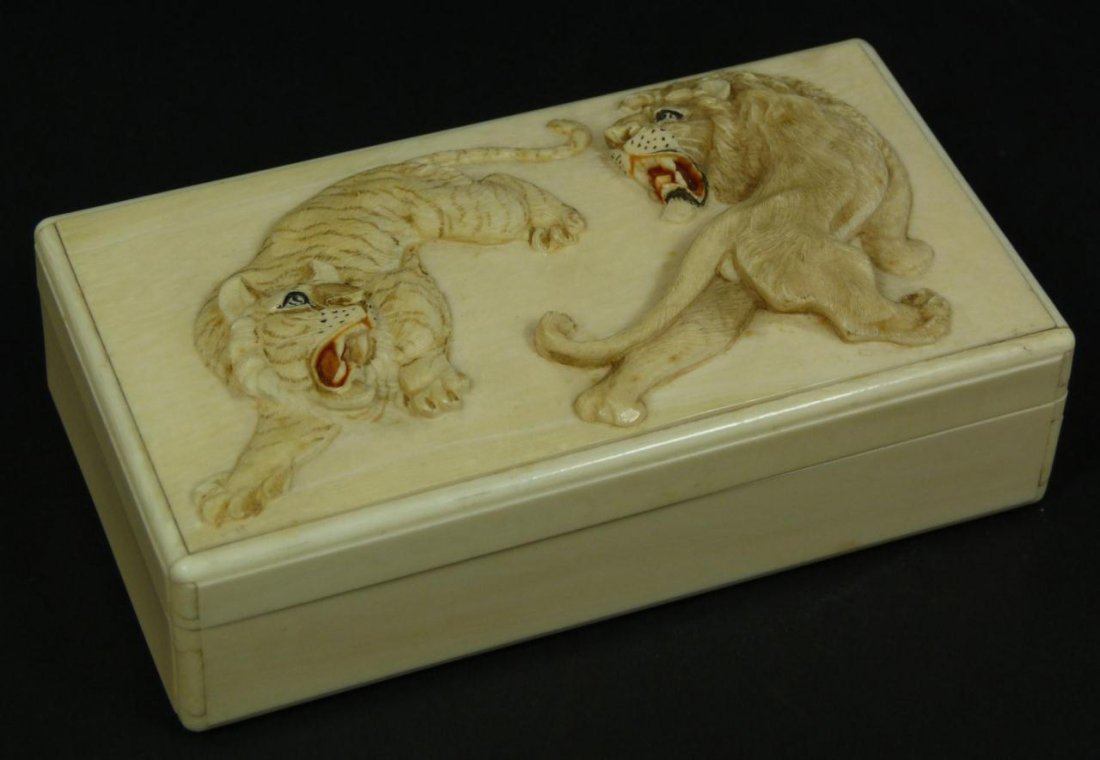 JAPANESE CARVED IVORY LION & TIGER BOX: A finely carved Japanese ivory rectangular form box having a high relief design to top depicting a lion versus a tiger. Each having polychromed red and black enamel highlights to mouth. 19th century. 